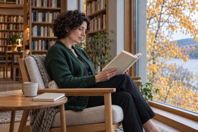 Læser med en åben bog ved et lyst biblioteksvindue
